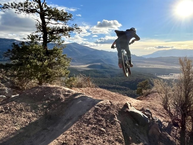 A mountain biker coming out of a jump onto a dirt trail.