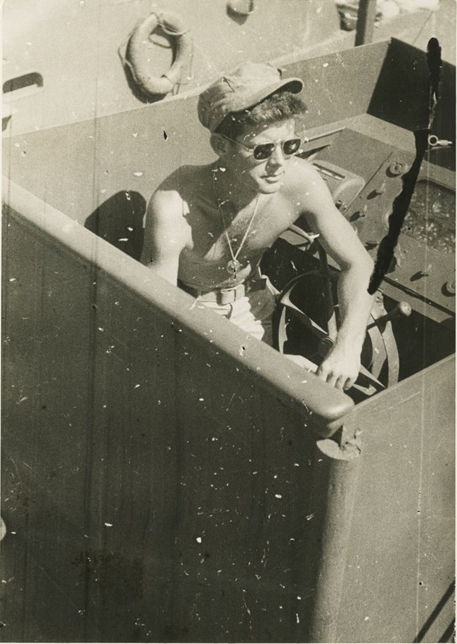 A smiling, shirtless Lt. John F. Kennedy in cockpit of PT-109