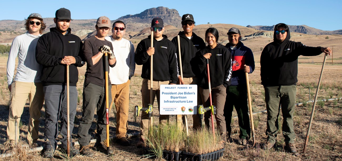 A group of young men and women hold tools in a high desert area.