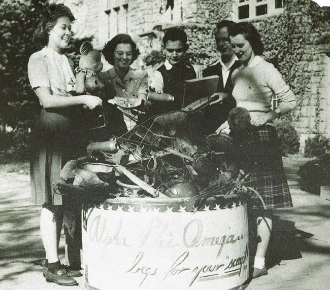 four college students - women and one man - gathered around a bin holding scrap for a scrap drive