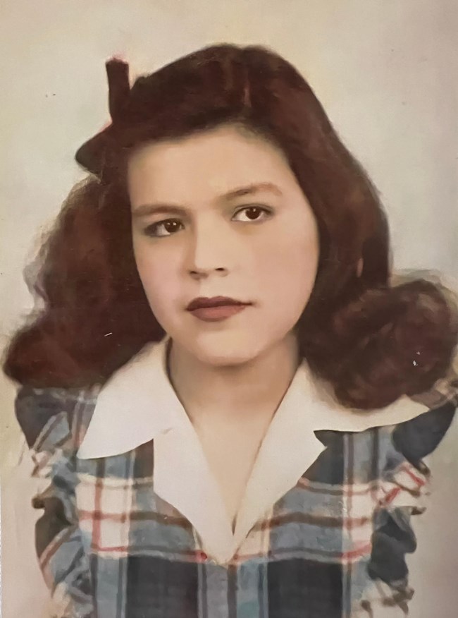 Josephine Delgado as girl courtesy Delgado family Hand colored portrait of a girl with a wavy, chestnut hair; a white shirt; and a plaid dress.