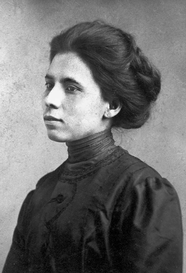 Jovita Idár Portrait of a woman with dark hair pulled back from her face wearing a dark top with a collar that goes all the way up to her neck. Photograph is taken from the chest up with the woman turned 45 degrees away from the camera.