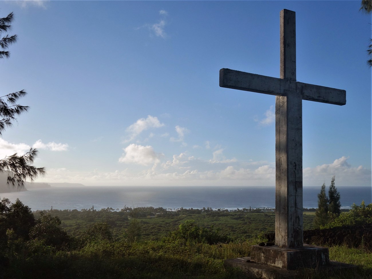 Monument of cross stands overlooking lush landscape below and sunrise over Pacific ocean