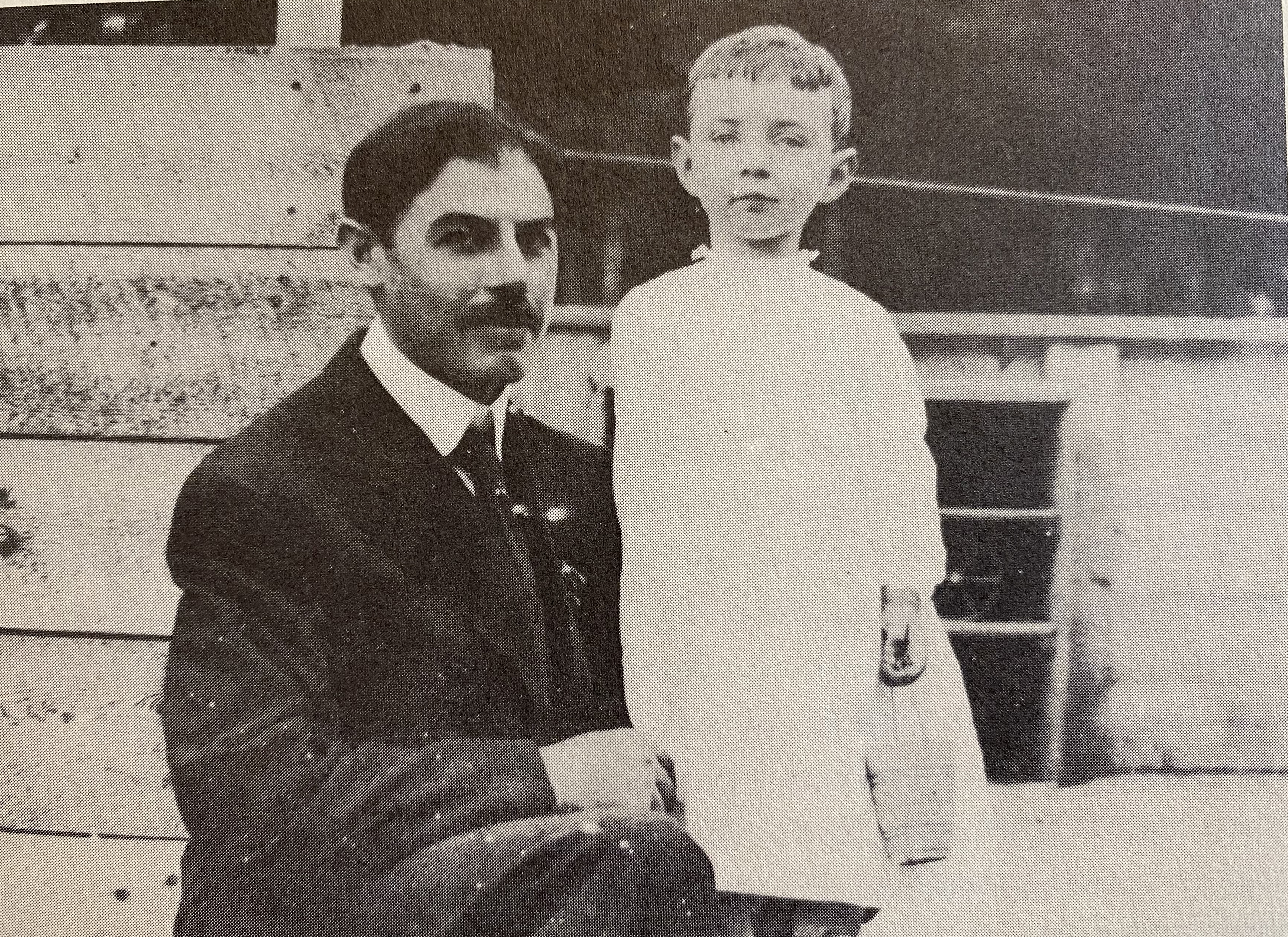 Black and white photo of a young Oppenheimer standing next to his seated father Julius.