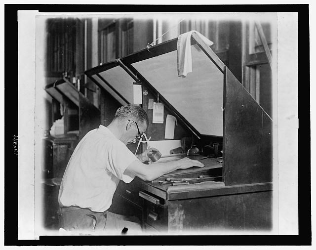 A worker lines up engraving plates inside a large open press