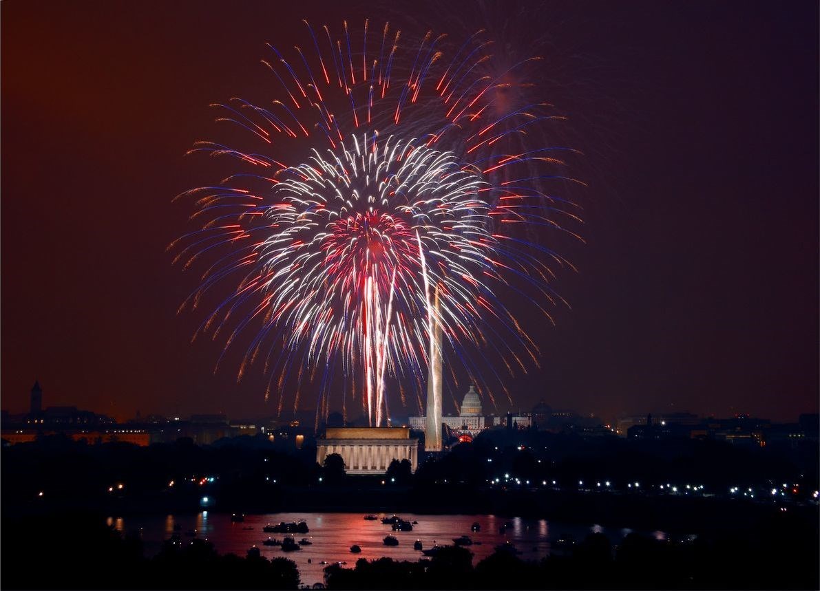 Red and purple fireworks explode over Washington D.C. at night, highlighting the Lincoln Memorial in the foreground
