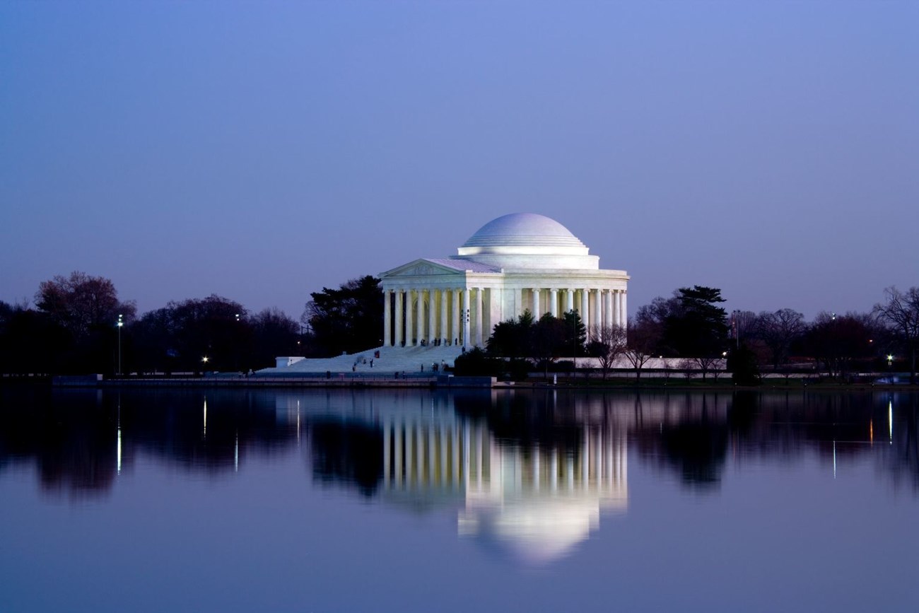 View at dusk over the water of the Tidal Basin toward the white domed building of the Jefferson Memorial