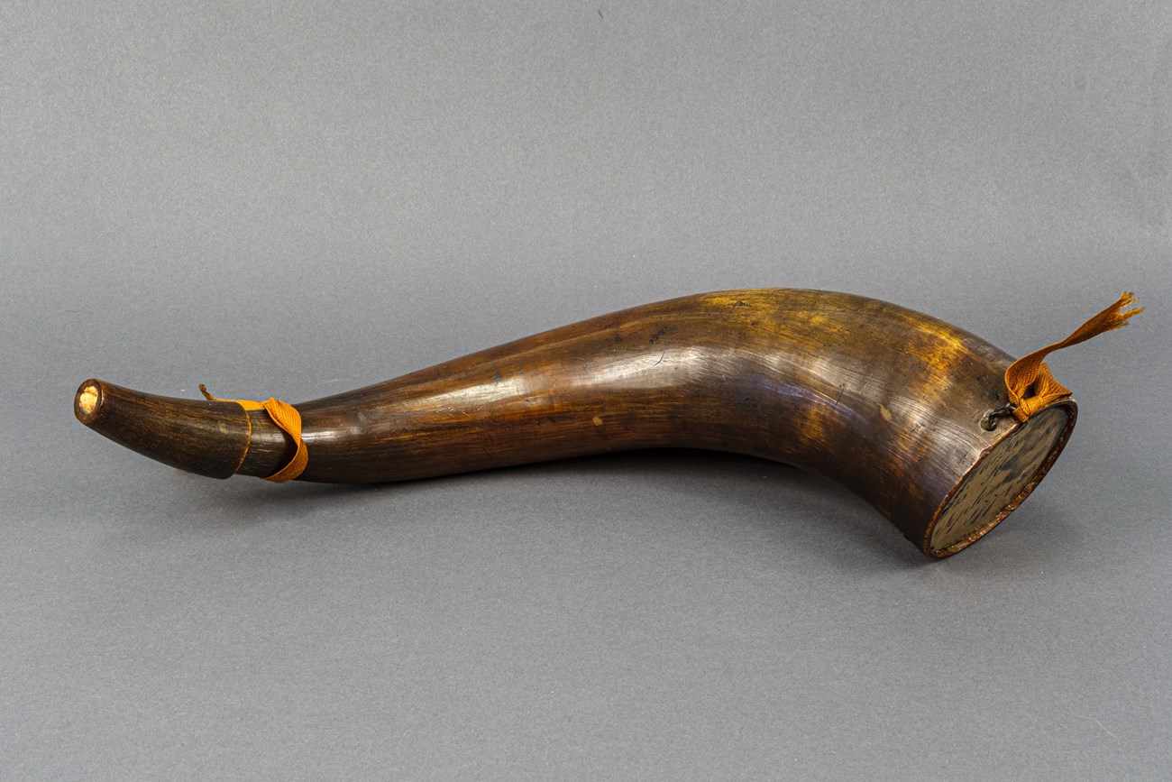 A brown and tan colored powder horn with orange ribbon tied at either end