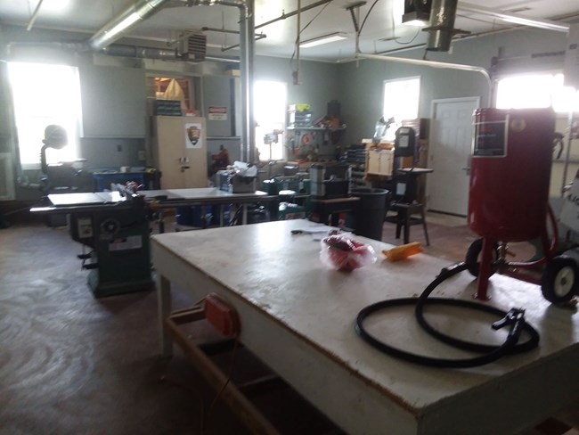 The interior of a workshop is pictured with tables, storage cabinets, and various tools.