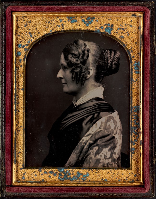 Daguerreotype of a side profile of a women with curled hair and a high collared dress