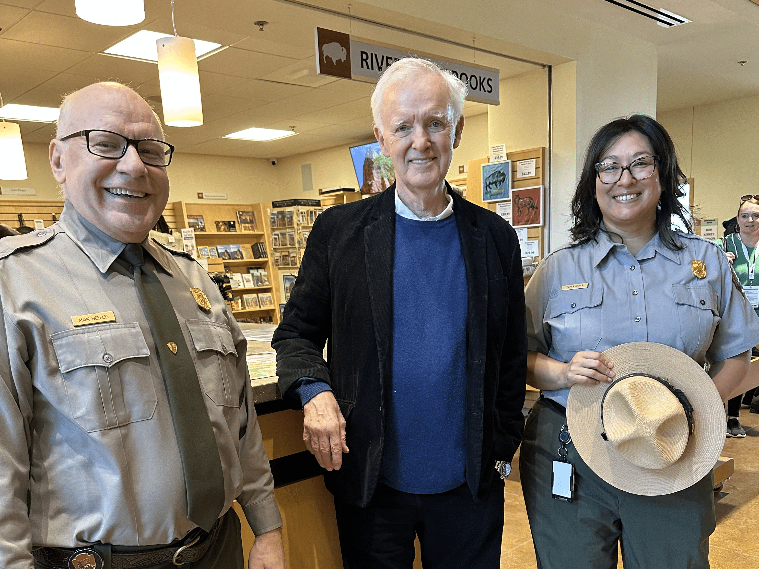 Two people in park ranger uniforms pose with a man in a visitors center