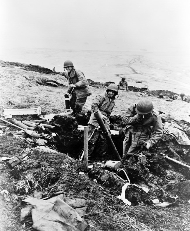 Three men in a hole with large metal guns throwing mortars