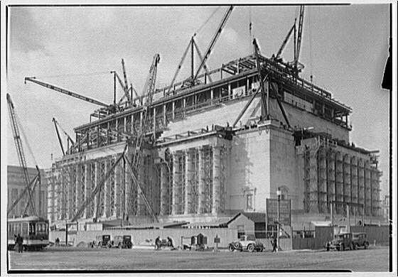 NAConstruction A large building with classical elements being constructed. Large columns line each side of the structure with scaffolding and cranes on the top of the building.