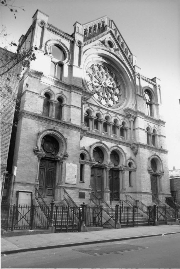 Black-and-white photograph of the synagogue, showing a large, centered rose window and horseshoe-shaped arches above the doors and windows.