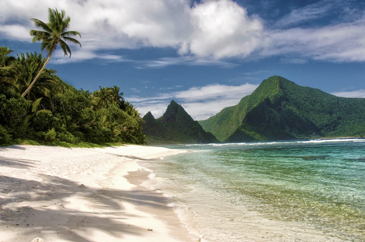 A sandy beach and vegetation-covered mountains of American Samoa