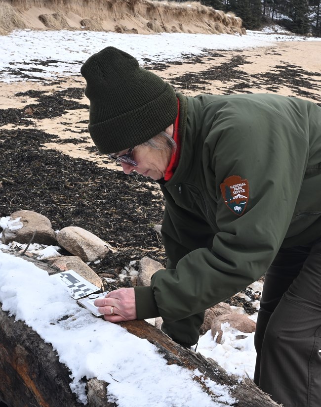 A park ranger kneels over to hammer tag into a piece of the shipwreck