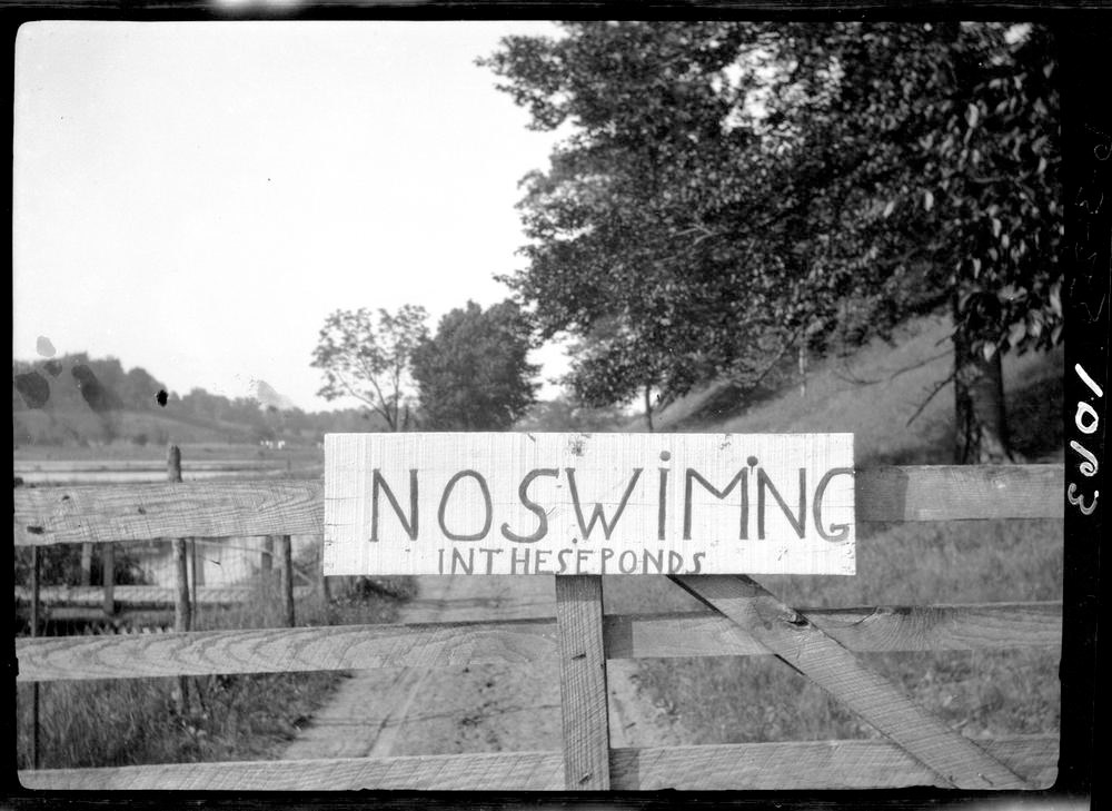Black and white photo with a sign reading "no swimming in these ponds"