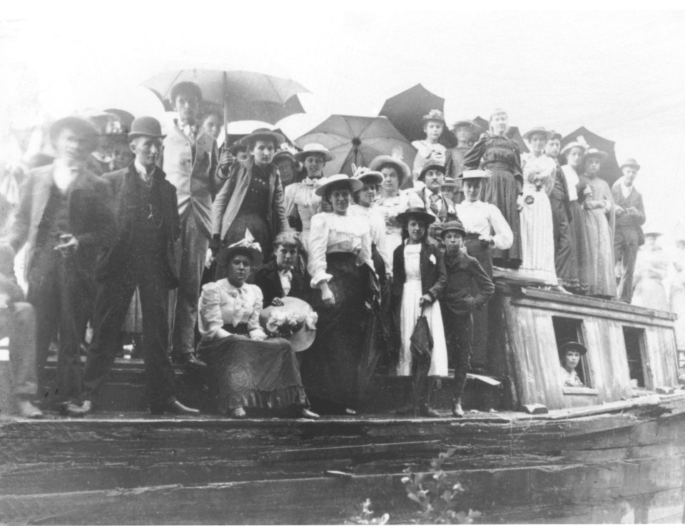 Historical black and white image of men, women, and children gathered on a canal boat.
