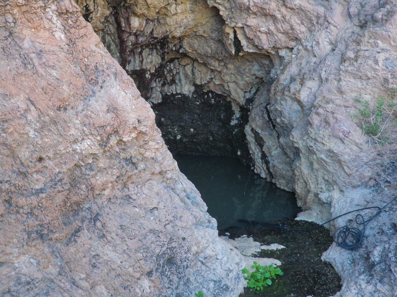 A dark pool of water sits deep in a crevasse between reddish-white rock.