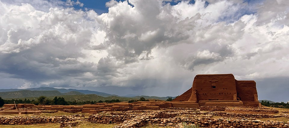 An old adobe church sits on a grassy plain surrounded by rubble.