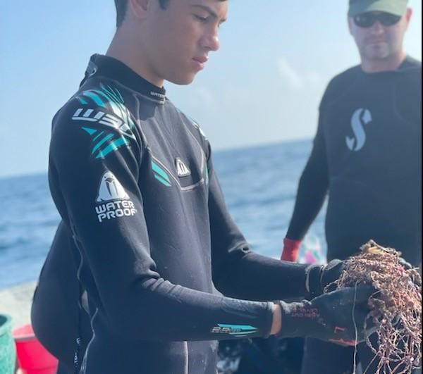 SCUBAnaut Alex Guirgues Young man wearing a black wetsuit on a boat with the ocean in the background