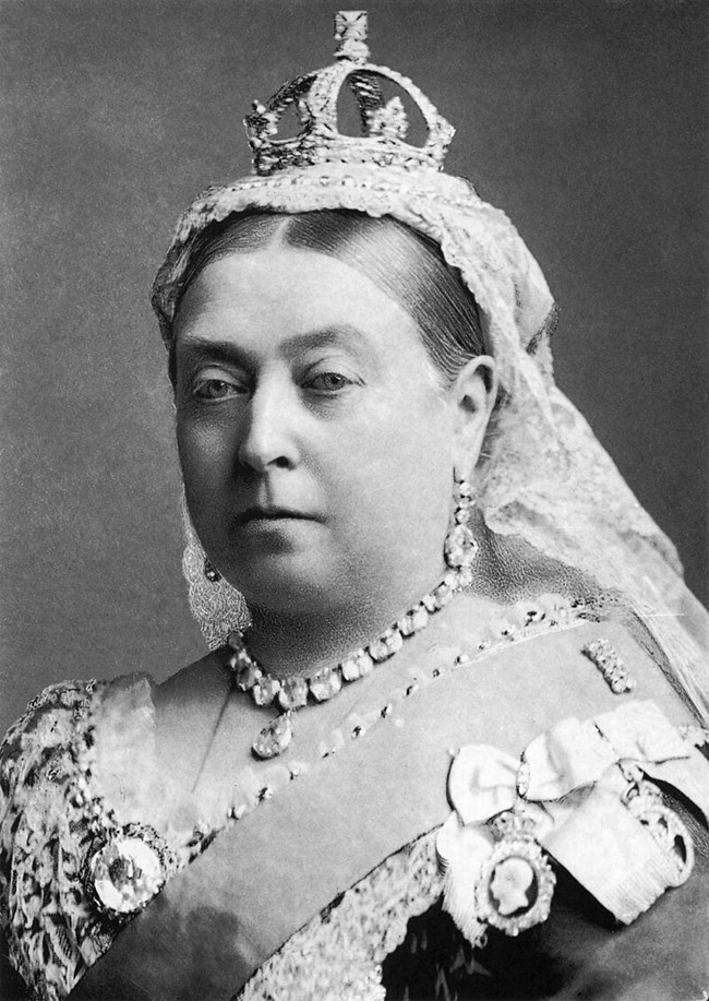 Woman wearing a crown, ornate jewlery, and a lavish dress.