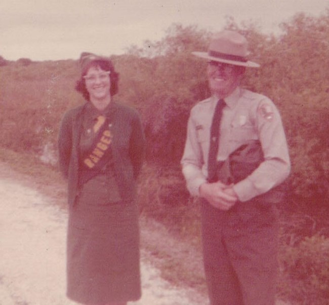 Rae O'Dell in her Girl Scout uniform with ranger aide sash stands on a trail next to ranger in uniform.