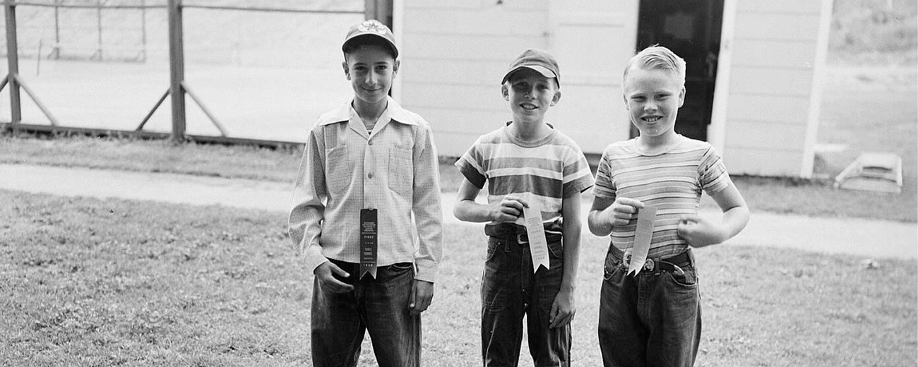 The young boys stand in a yard holding ribbons.