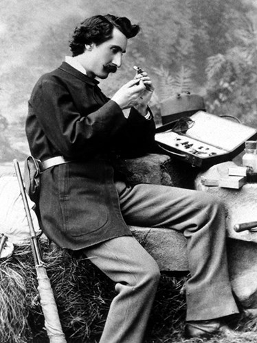 Riley_USDA black and white photo of a seated nineteenth century man inspecting a small object in his hands. He has