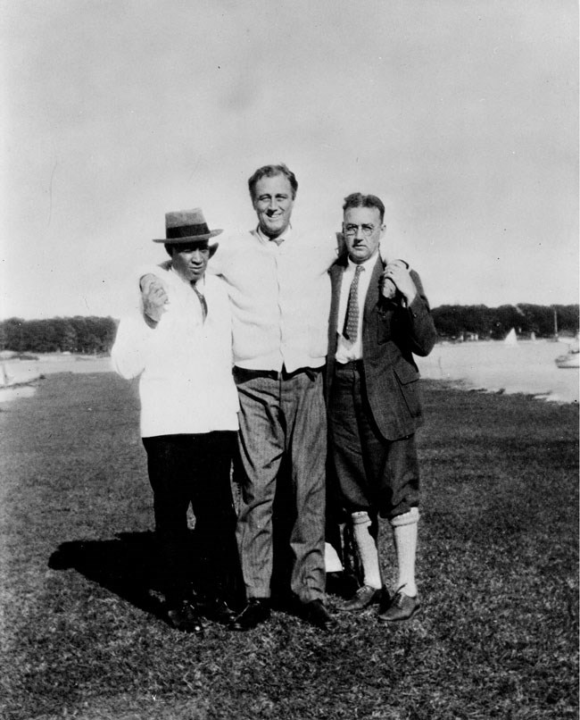FDR standing and supporting himself with his arms round the shoulders of Leroy Jones and Dr. McDonald.