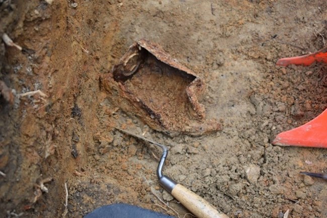 A Tin Can Associated with a Civil War Trash Deposit. NPS Photo A rusty tin can sitting in the middle of an open dirt unit with a metal trowel and red plastic shovel near it.