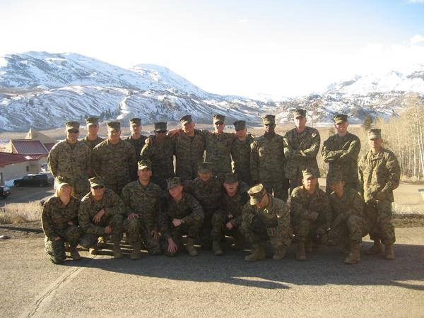 A group of marines pose for a photo with snow covered mountains in the background.