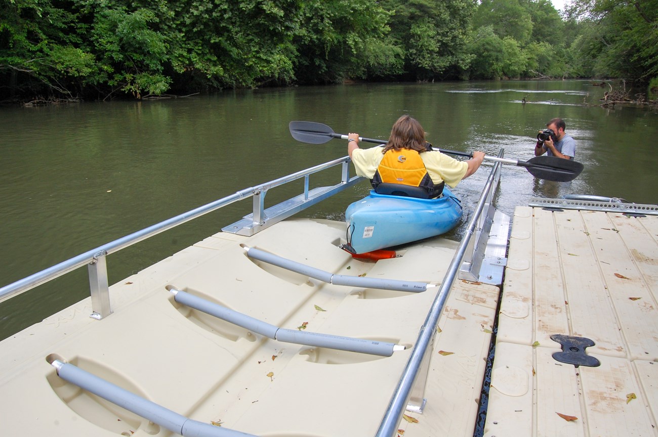 Paddler uses a wheelchair accessible kayak launch dock to enter the water.