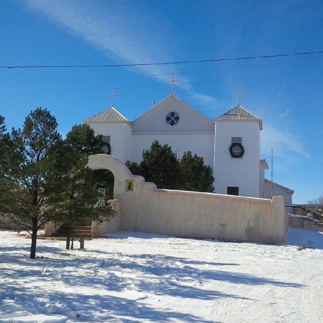 A large white stone church with two bell tours, in the snow.