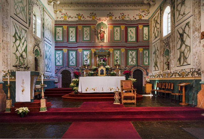 Brightly painted altar with poinsettias on both the floor and on tables. Two doors on either side of the central altar table.