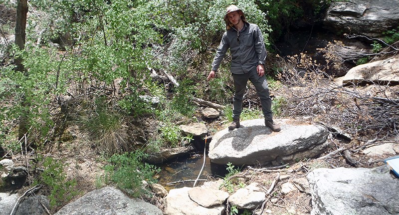 A person pointing at a small pool of water surrounded by large rocks in a drainage.