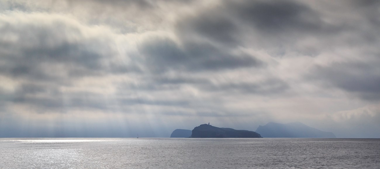 Islands on the ocean horizon, with light streaming down through clouds