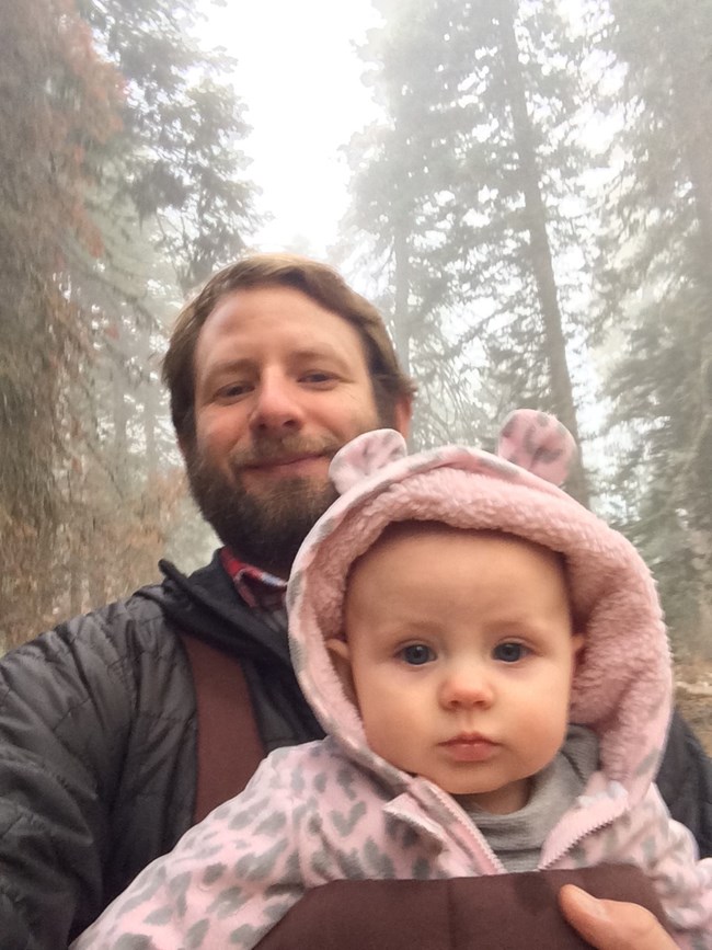 Man holds his toddler in front of him in the forest.