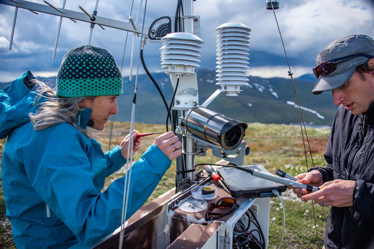Climate scientists repair climate station. Mountains in the backdrop.