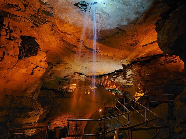 A cascade of water enters a cave passageway from the ceiling. A cascade of water enters a cave passageway from the ceiling.