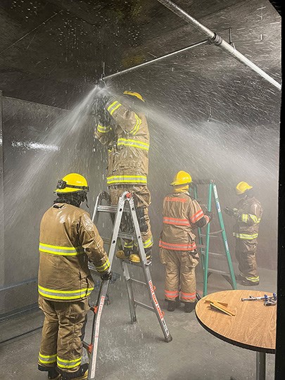 Firefighters stand under a sprinkler spraying water.