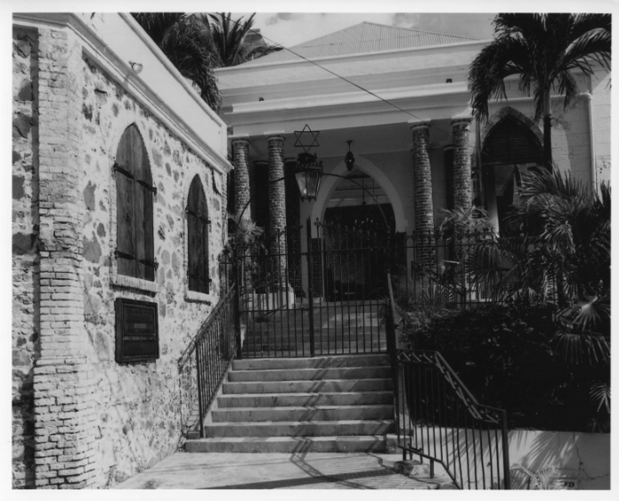 A series of steps lead up from the street to a wrought iron gate and fence. The gate, surmounted by a wrought iron Star of David, gives access to a paved forecourt fronting the St. Thomas Synagogue and its entrance under a roofed porch. Synagogue is a rec