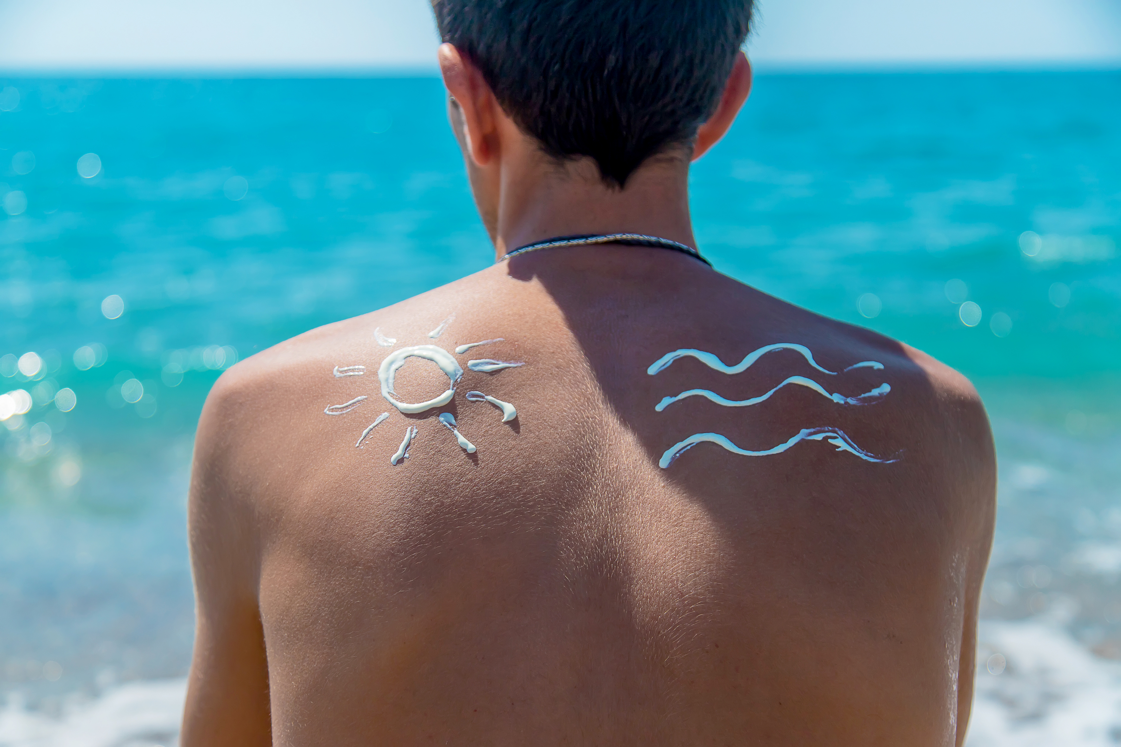 a man with sunscreen art on his back looks at a turquoise ocean.