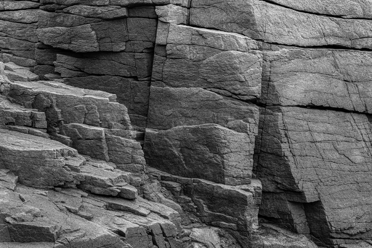 Black and white study of light, shape, and fractures in a stone cliff face.