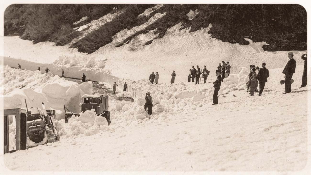 A group of people on snow, watching snow removal operations