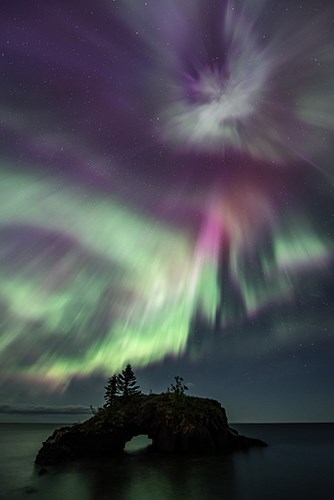 Swirling purple and green aurora behind an island arch formation silhouette.