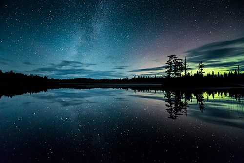 Silhouette of land dividing a glowing night sky from its reflection.