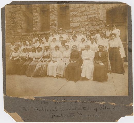 Sepia photo with three rows of Black women in dresses and long skirts of varying shades.