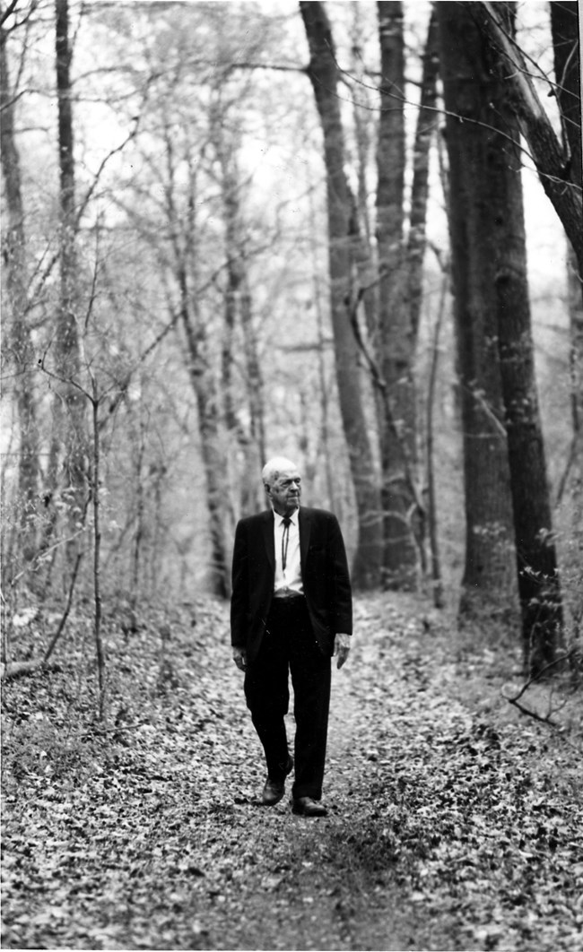 Freeman Tilden in a suit walks along a wooded trail