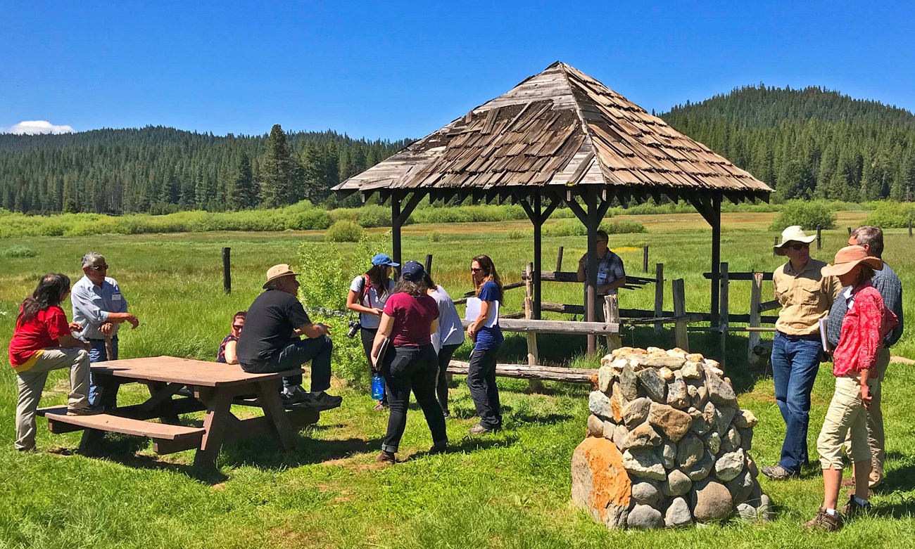 A group gathers at an interpretive site with a wooden gazebo at a sunny and grassy Yellow Creek Campground.